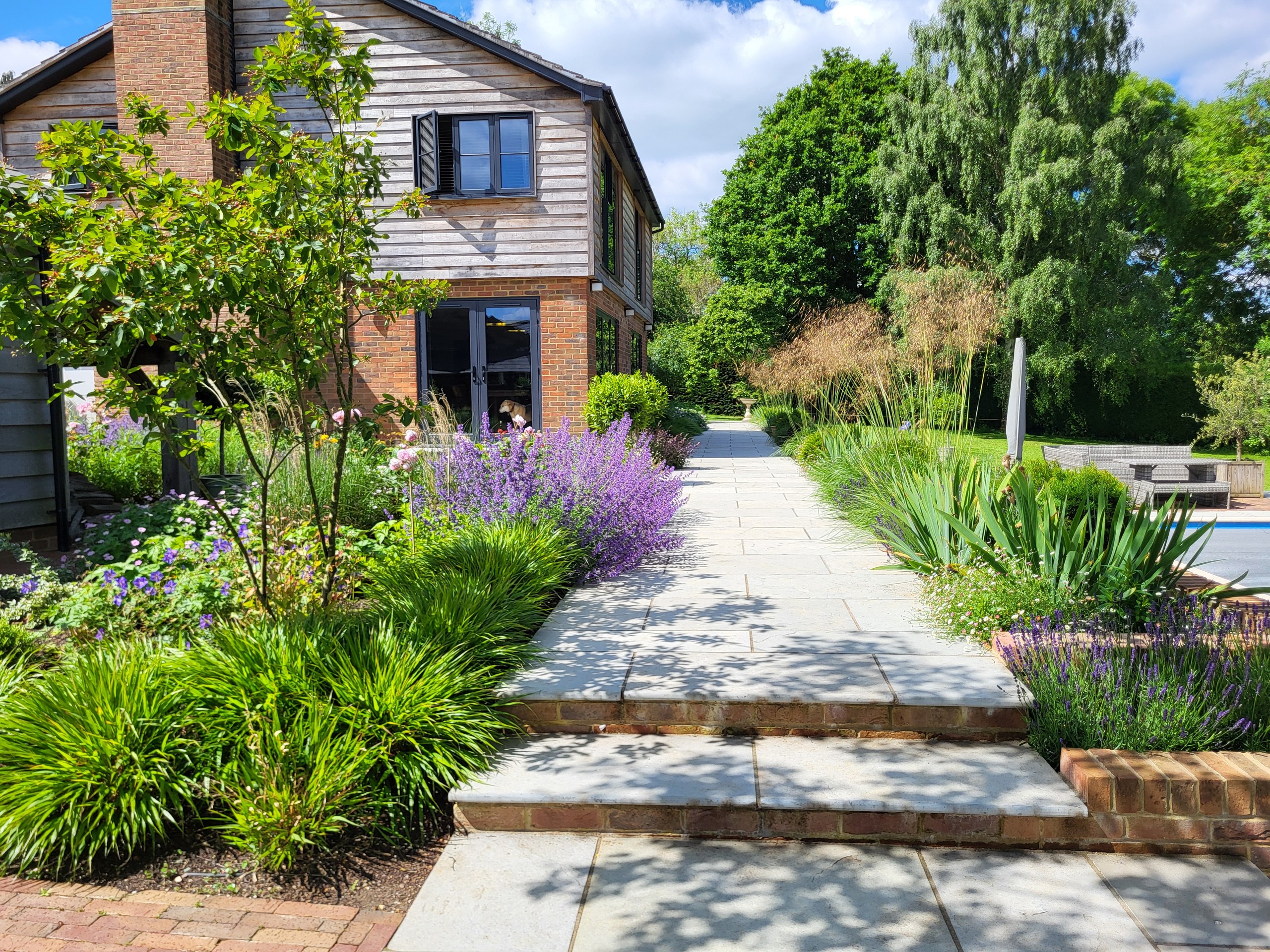 Shallow stone steps leading to a garden path between planted borders beside the house in Benenden.