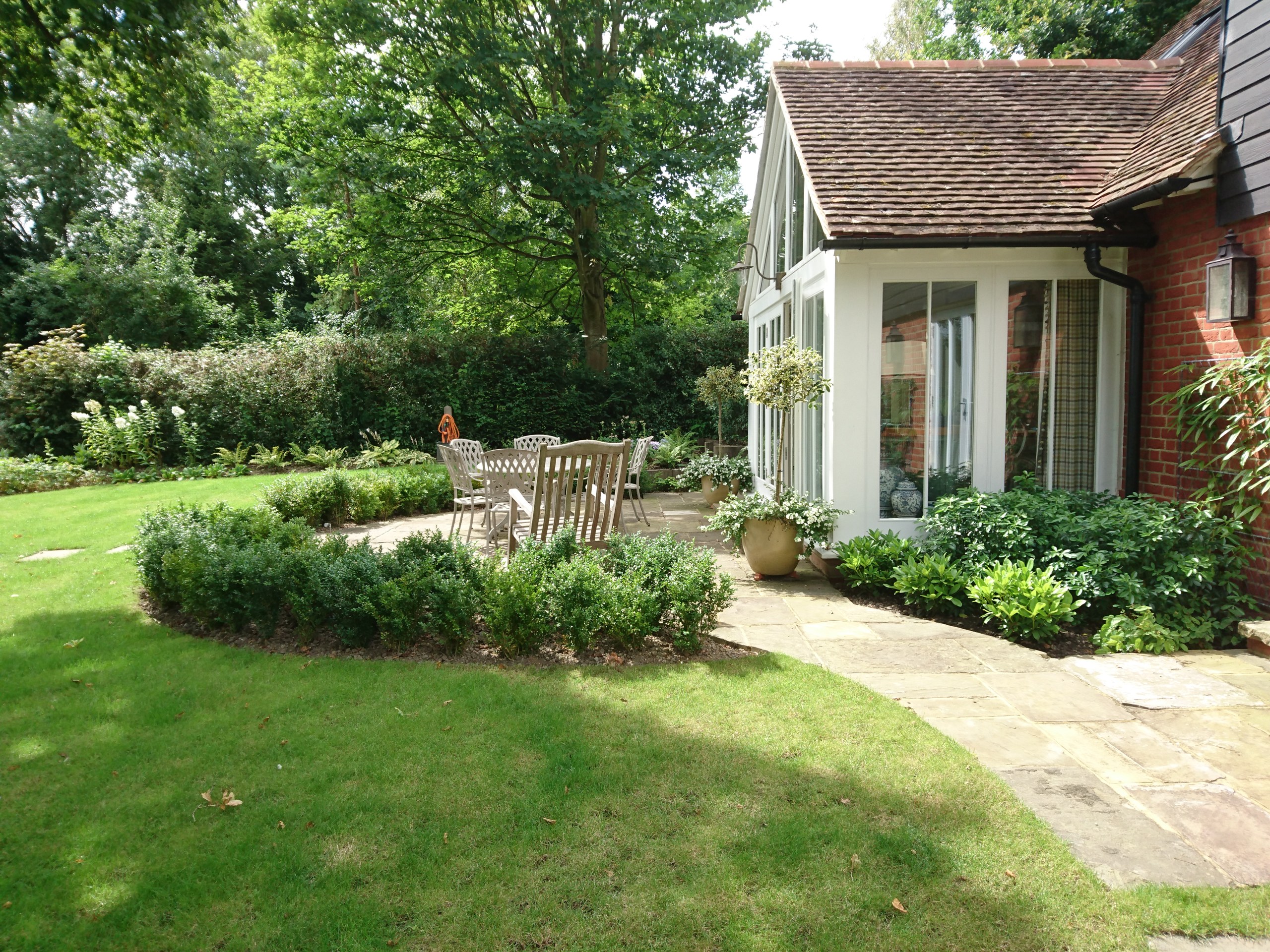 Curved stone patio and wooden dining furniture beside a glazed house extension and lawn in Cranbrook.