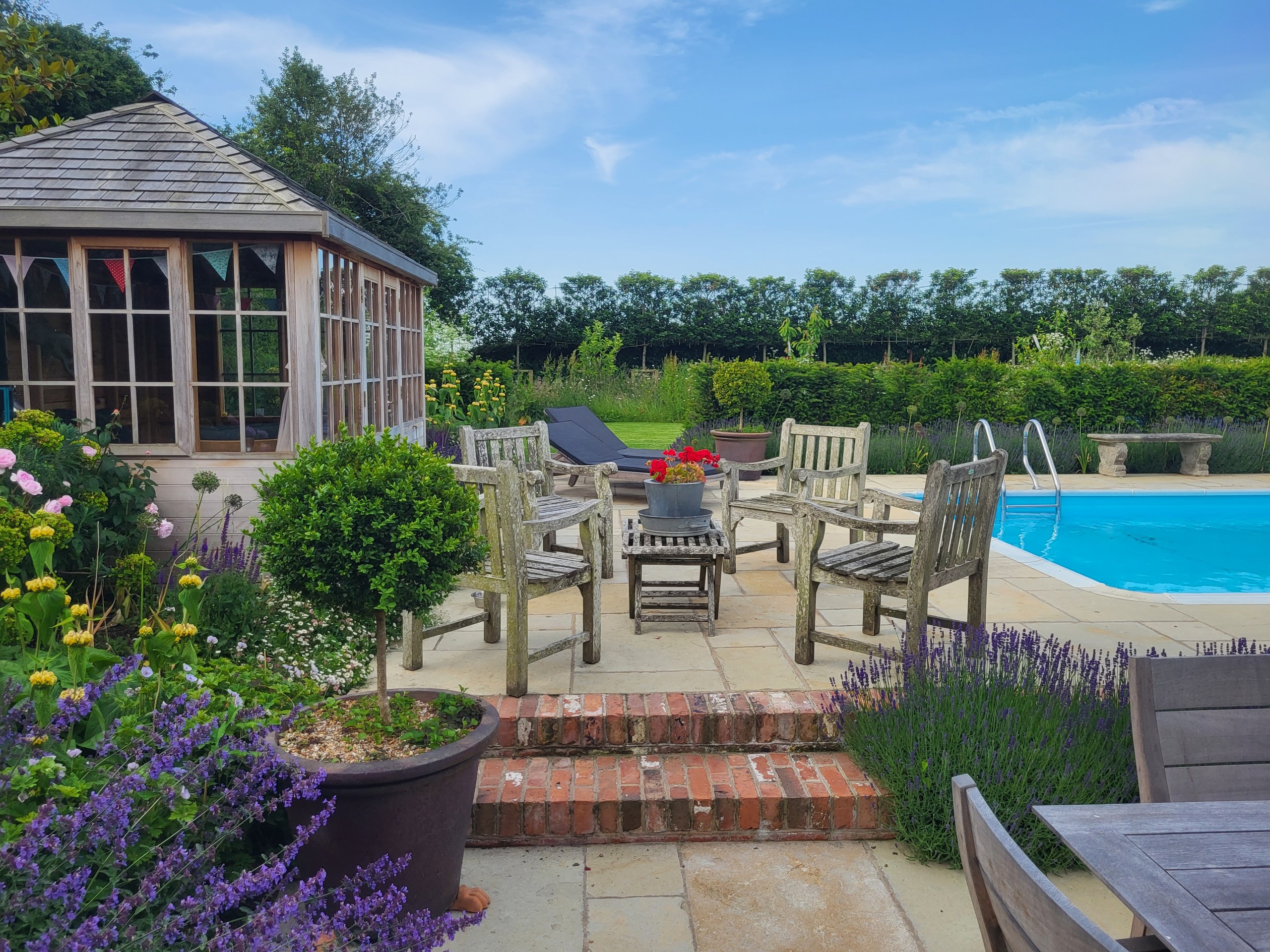 Brick steps leading to poolside wooden seating beside a summerhouse and planted pots at Holly House in Goudhurst.