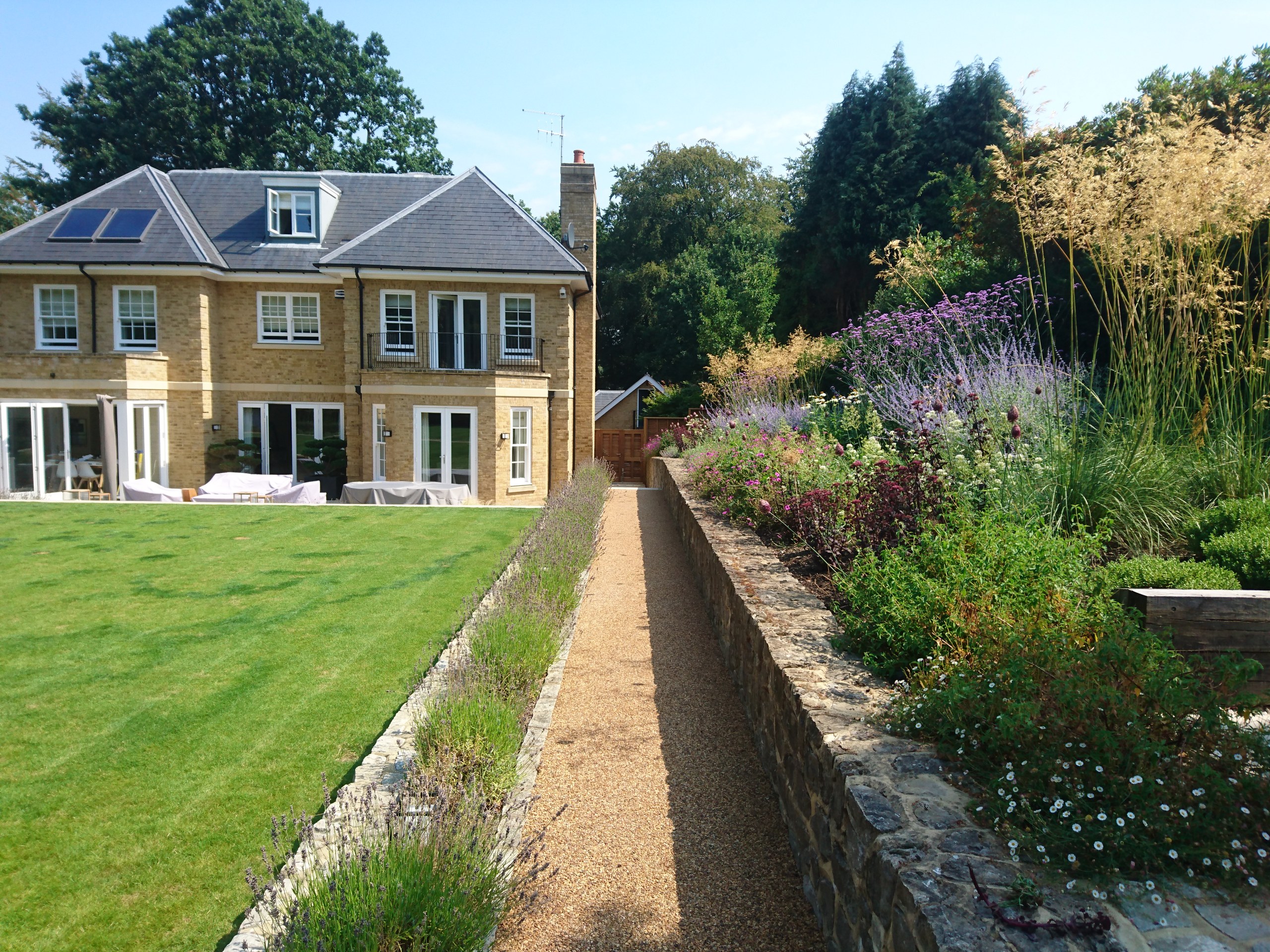 Gravel path beside a raised flowering border and lawn leading towards the house in Sevenoaks.