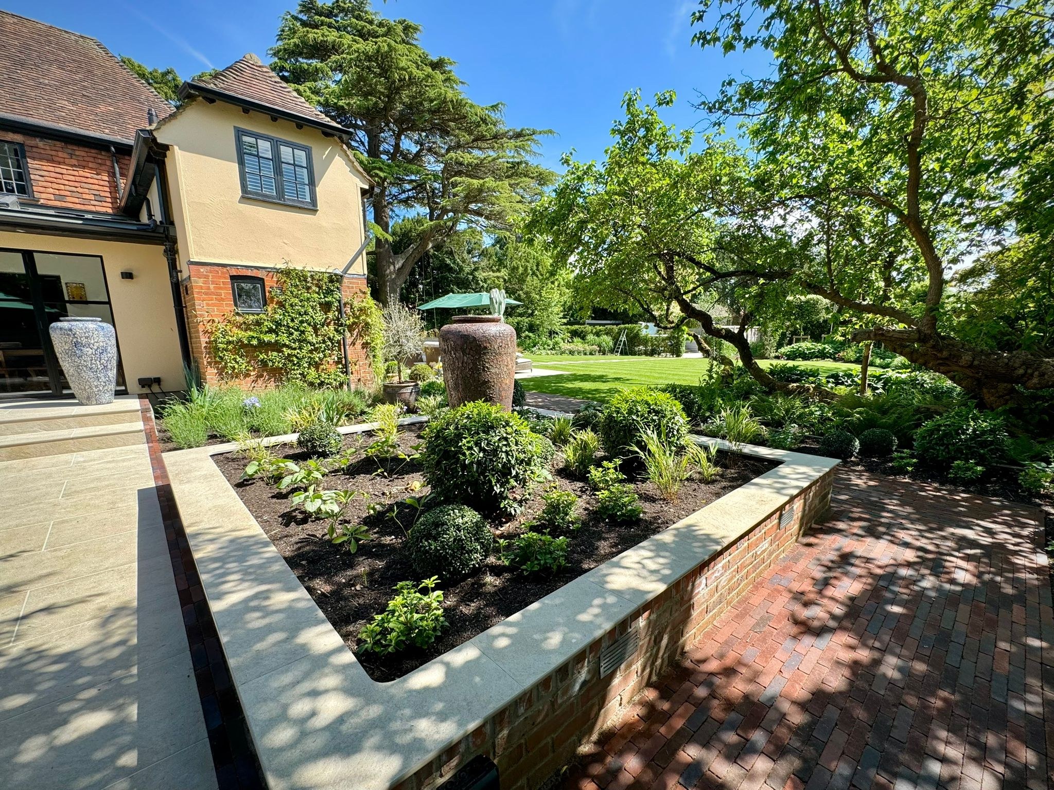 Raised brick planter with pale stone coping beside a garden terrace and mature tree in Yalding.