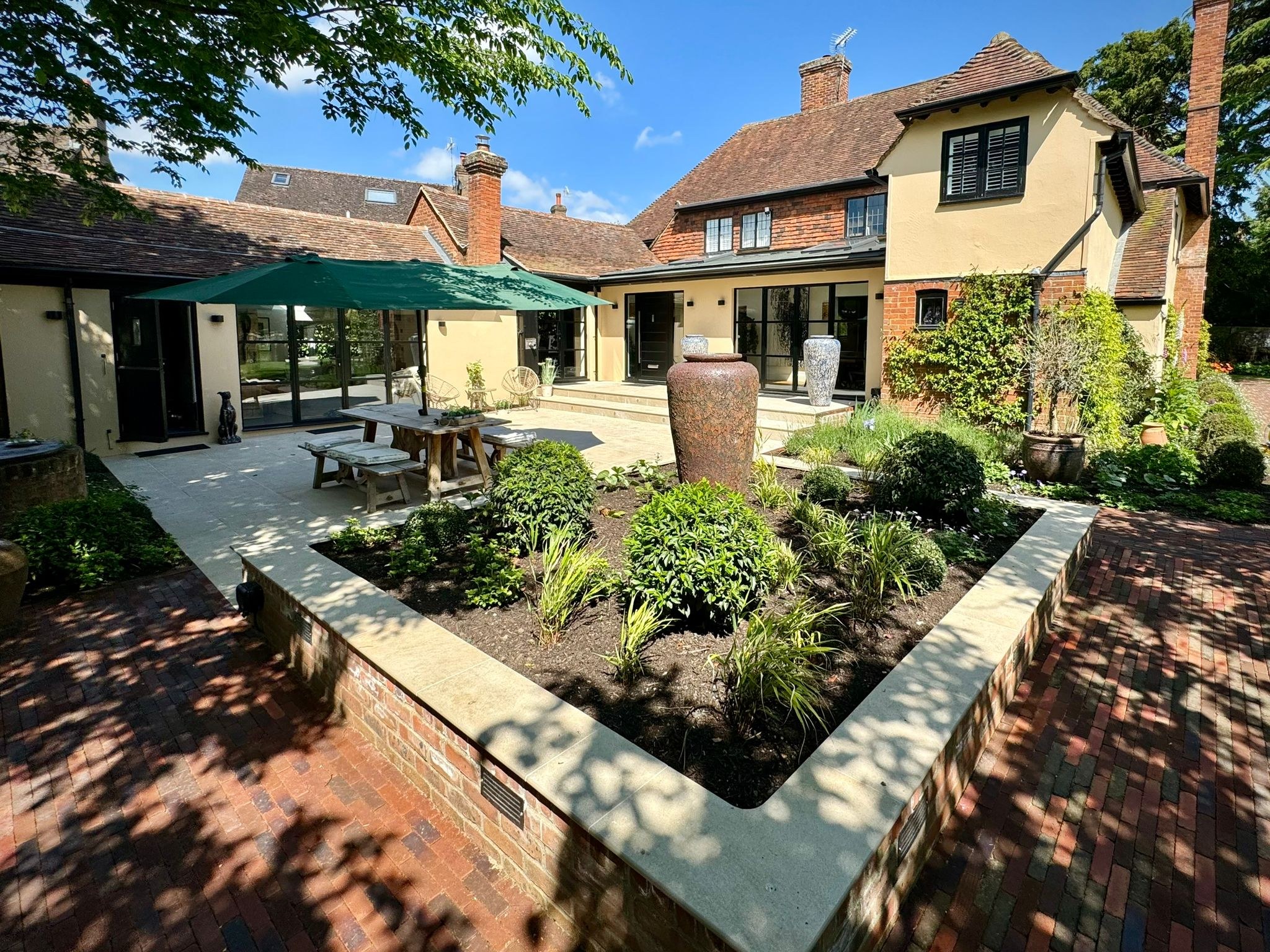 Raised brick planter with clipped shrubs and a tall urn beside a paved courtyard in Yalding.